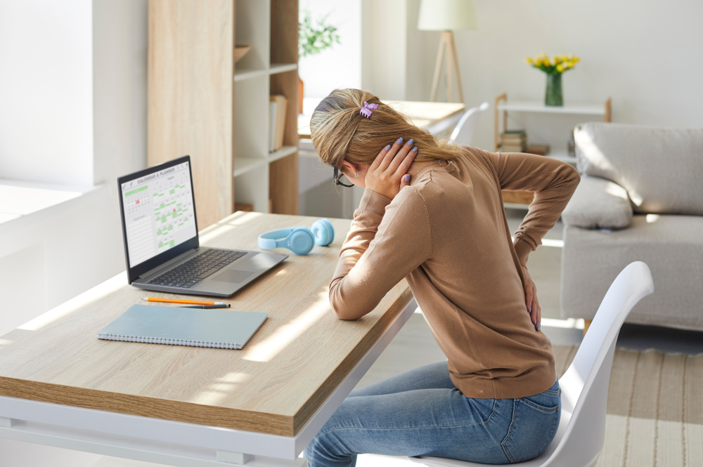 Frau am Laptop mit Rückenschmerzen