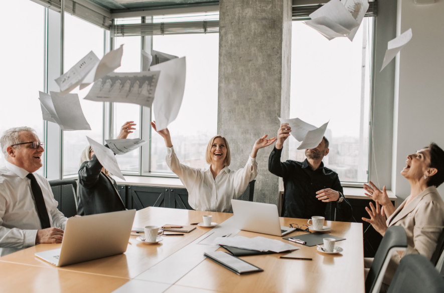 Mitarbeiter sitzen im Büro beim Meeting und lassen beschriebene Blätter fliegen