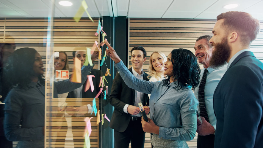Mitarbeiter vor einer Glaswand, an der Post-its kleben